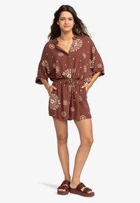 Romper marrone a fantasia con maniche corte, vita regolabile con coulisse e tasche; il tessuto ha una texture leggera e una vestibilità comoda.