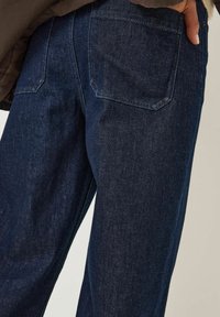 Tmavě modré džínové kalhoty s hladkou texturou, které mají dvě zadní kapsy, rovný střih a jemný lesk.