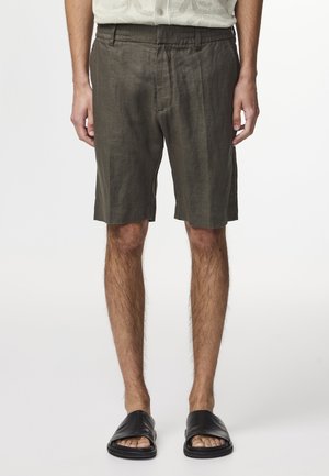 Leinen-Shorts in dunkelolivgrün mit entspannter Passform, ausgestattet mit Seitentaschen und einer glatten Textur. Kombiniert mit schwarzen Rutsch-Sandalen.