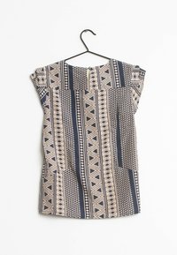 Tunique bleu marine et beige à motifs avec des designs géométriques, manches courtes, encolure ronde et fermeture à boutons au dos. Accrochée à un crochet noir.