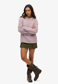 Różowy sweter o melanżowym wzorze z luźnym krojem, okrągłym dekoltem i prążkowanymi mankietami, w zestawie z zieloną spódnicą cargo i brązowymi kozakiem do kolan.