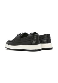 Sneaker in pelle nera con suola bianca texturizzata, caratterizzate da dettagli in rilievo e design minimalista. La vista posteriore mette in evidenza la finitura liscia.