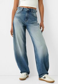 Ljusblå, högmidjade jeans i denim med en lös, vida benpassform. Har subtil blekning och synliga sömmar. Kombineras med vita sneakers.