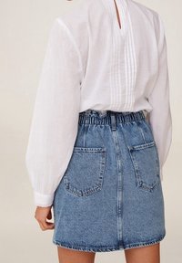 Blouse blanche légère à manches bouffantes et pli au dos, associée à une jupe en denim bleu taille haute avec deux poches arrière.