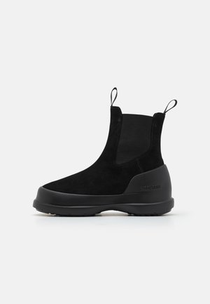 Stivaletto in suede nero con pannelli laterali elastici, linguette superiori e una suola in gomma spessa. Design minimalista con punta rotonda.