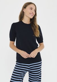 Tumši zils adīts tops ar apaļu kakla izgriezumu un īsām puftīgu piedurknēm, kombinēts ar melnām un zilām svītrainām biksēm. Gluda tekstūra, pieguloša forma.