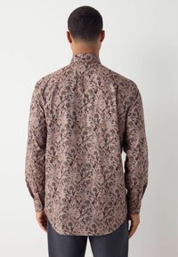 Camicia a maniche lunghe in tessuto leggero con uno sfondo rosa e intricati motivi floreali scuri. Vestibilità su misura e polsini con bottoni.