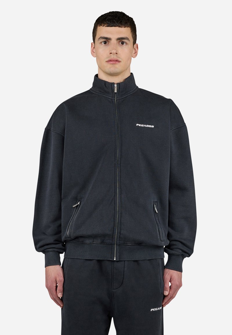 Sweatshirt cinza escuro com fecho, gola alta, punhos canelados e dois bolsos frontais com fecho. Apresenta o logótipo branco "PEGAADOR" no peito.