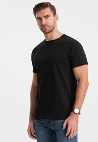 Sort kortærmet t-shirt i en tætsiddende design, lavet af blødt bomuld. Casual look parret med blå jeans og et minimalistisk armbåndsur.