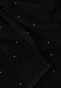 Tissu en maille noire avec détails de poignets froncés et petits strass argentés dispersés en tant qu'accents décoratifs.