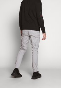 Lichtgrijze cargobroek met elastische boorden, meerdere zijzakken en een comfortabele pasvorm, gecombineerd met een zwart shirt met lange mouwen.