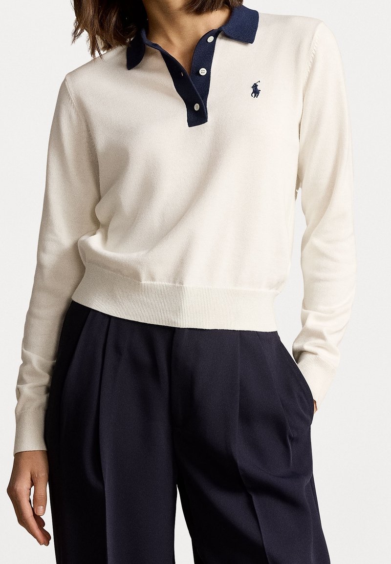 Pull en tricot crème avec un col marine, arborant un petit logo sur la poitrine. Le design comprend des poignets et un ourlet côtelés pour un meilleur ajustement.