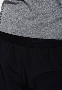 Top atlético gris combinado con pantalones cortos negros, con una textura suave y una cinturilla elástica con una marca impresa en el lateral.