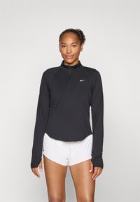 Black long-sleeve athletic top with a half-zip collar and a white Nike logo, paired with white shorts. Smooth fabric, fitted design.