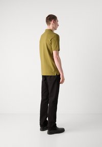 Polo de manga corta verde oliva, diseño ajustado, combinado con pantalones negros y zapatos negros, visto desde la parte trasera sobre un fondo neutro.