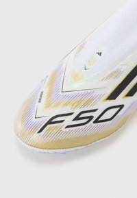Calzature con una tomaia sintetica bianca, con accenti dorati e viola, motivi angolari netti e un logo "F50" nero.
