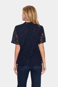 Tumesinine pitsist ülikond, lühikeste varrukatega, lillemustriga, ümmarguse dekoltee ja peplum-tuhmusega, koos tumesiniste teksadega.