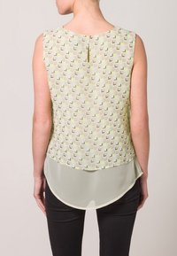 Blusa senza maniche con una parte frontale in leggero verde a motivo geometrico. Orlo posteriore trasparente, bordo inferiore arrotondato e chiusura a chiave.