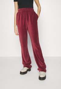 Karmosinröda flanellbyxor med elastisk midja, sidofickor och en avslappnad passform. Benen smalnar något av mot mudden.