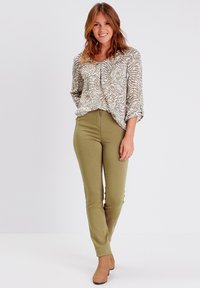 Blouse imprimée avec un motif zèbre beige et crème, associée à un pantalon ajusté vert olive et des escarpins beiges. Tissu lisse avec une coupe décontractée.