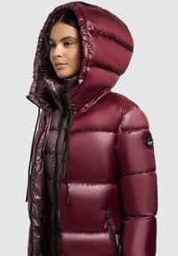 Burgundy puffjacka med stor huva, dragkedja fram, elastiska snören och sidofickor. Slät, glansig material med ett quiltat mönster.