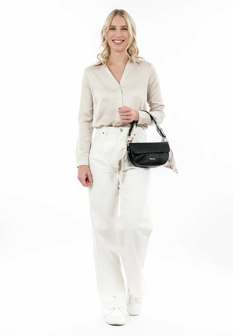 Black leather handbag with a curved shape, short handle, and floral scarf accent. Model wears a beige blouse and white wide-leg pants.