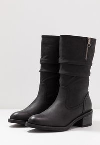 Svarta faux läderankelboots med en vikbar topp, sidodragkedja och låg klack. Slät textur med subtila sömnadsdetaljer.