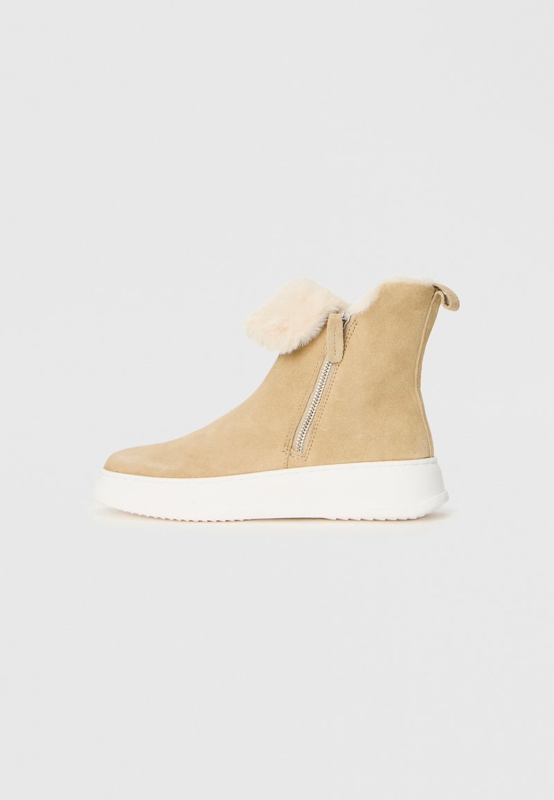Beige mockasinstövel i mocka med vit gummisula, sidodragkedja och vikt krämfärgad färg.