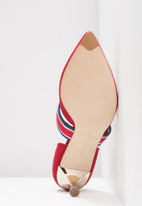 Chaussure à talon haut en suede rouge avec un bout pointu, dotée d'un talon métallique doré et d'accents en tissu rayé rouge, blanc et marine. Semelle lisse.