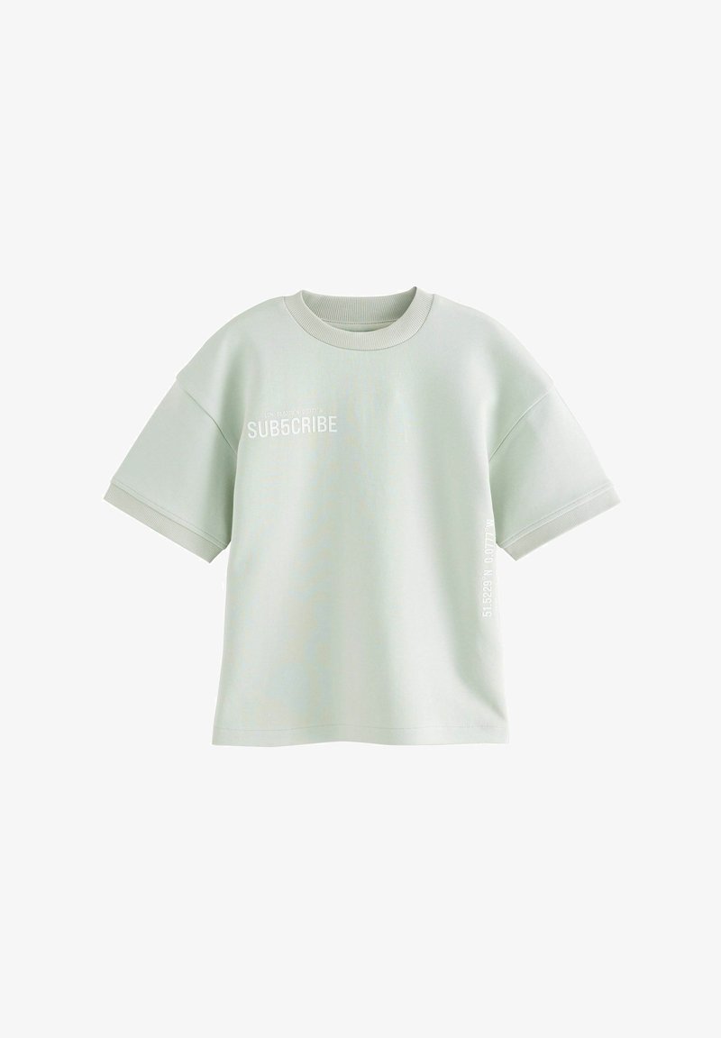 Šviesiai žalios spalvos per didelis marškinėlis, pagamintas iš minkštos medvilnės, su trumpomis rankovėmis ir baltais užrašais, kurie sako "PRENUMERUOK" priekyje ir šone.