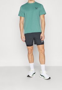 Minttuvihreä lyhythihainen t-paita, jossa on pieni musta logo, yhdistettynä mustiin urheilushortseihin ja valkoisiin lenkkikenkiin, joissa on vihreitä yksityiskohtia ja paksut valkoiset sukat.