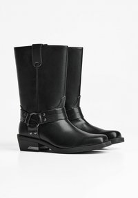 Pair of black mid-calf leather boots with low stacked heels and decorative harness straps and metal rivets.