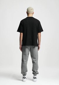 Svart bomull T-skjorte med korte ermer, kombinert med grå joggebukser og hvite sneakers med svarte detaljer. Utsikt fra baksiden.
