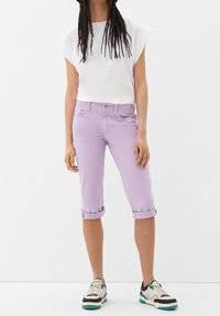 Light purple cropped pants with rolled cuffs, paired with a white short-sleeve top and black, green, and white sneakers.