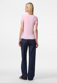Camiseta rosa de canalé con bordes festoneados combinada con jeans de mezclilla azul de pierna ancha y cintura alta. La vista posterior muestra una textura suave y un ajuste relajado.