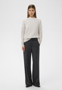 Light gray wool sweater with round neckline, paired with dark gray wide-leg trousers, highlighted by a black belt and subtle side pockets.
