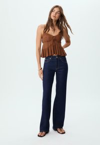 Camisole cropped marron, texturé, avec un ourlet peplum, associé à un jean large taille haute, bleu foncé, avec des détails de couture contrastés.