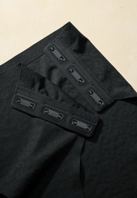 Black fabric with a textured pattern. Two sections feature black hardware accents and stitching, including snapped closures.