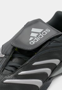 Crna sportska cipela sa sivim detaljima, teksturirane površine, s vezicama i logotipom Adidas na jeziku.