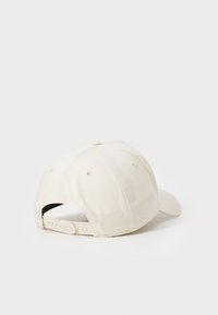 Cream baseball cap with a curved brim, made of fabric. Features ventilation eyelets and an adjustable strap at the back.