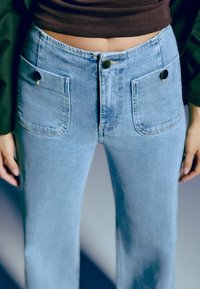 Personne portant un jean taille haute bleu clair avec des poches plaquées devant et un bouton, associé à un top court noir.