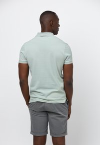 Ljusgrön kortärmad polo av slät tyg, matchad med grå shorts. Skjortan har traditionell krage och en figurnära design.