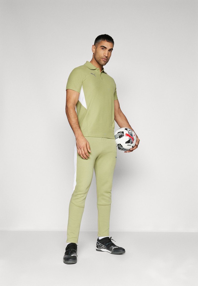 Gray polo shirt with green accents, paired with olive green joggers featuring white side stripes. Black athletic shoes and a soccer ball.