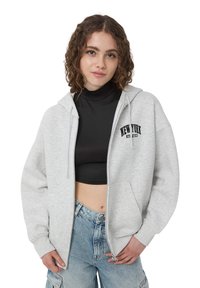 Felpa grigia con zipper realizzata in materiale morbido, presenta una tasca frontale e la scritta "NEW YORK ATHLETICS" in nero. Fit ampio, cappuccio con coulisse.