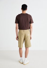 Brown cotton t-shirt and khaki shorts with back pockets and a small logo tag. White sneakers with cushioned soles visible. Simple design and fit.