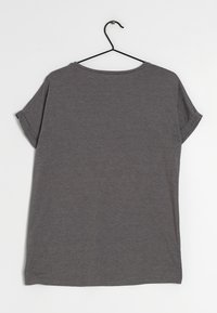 Camiseta gris de manga corta hecha de una tela suave, con cuello redondo y puños enrollados. Cuelga de un gancho negro sobre un fondo claro.