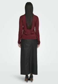 Bordeaux lange mouw trui gecombineerd met een zwarte denim maxi rok met gele stiksels, gedragen met zwarte hoge hakken.