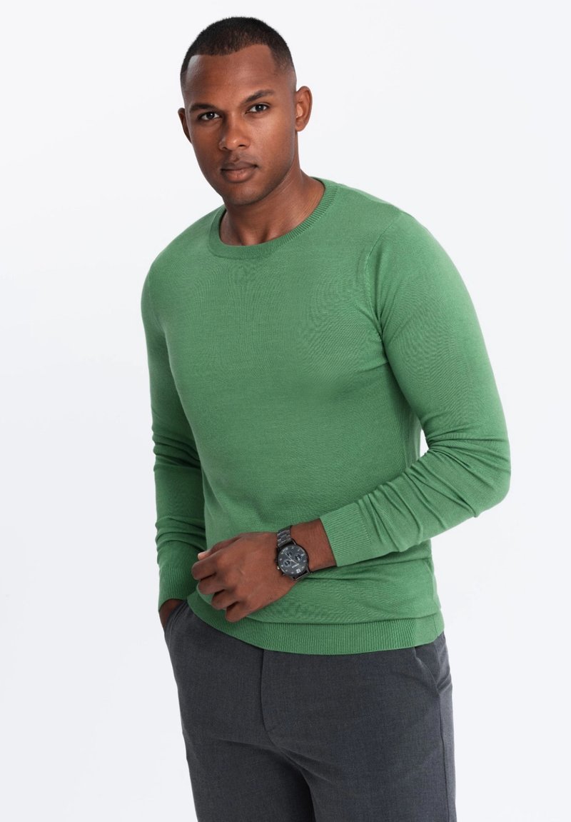Grüner langärmliger Pullover mit Rundhalsausschnitt, gerippten Bündchen und Saum. Tragen über grauen Hosen mit strukturiertem Finish.