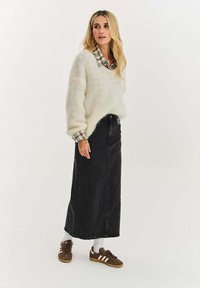 Krémový nadýchaný svetr s opuštěnými rameny přes kostkovanou košili, kombinovaný s dlouhou černou džínovou sukní a hnědými teniskami s bílými pruhy.