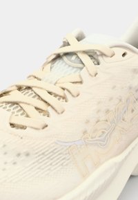 Shoe sportiv bej deschis, cu un superior din plasă, închidere cu sireturi, logo HOKA într-o nuanță subtilă de galben și o talpă texturată pentru tracțiune.